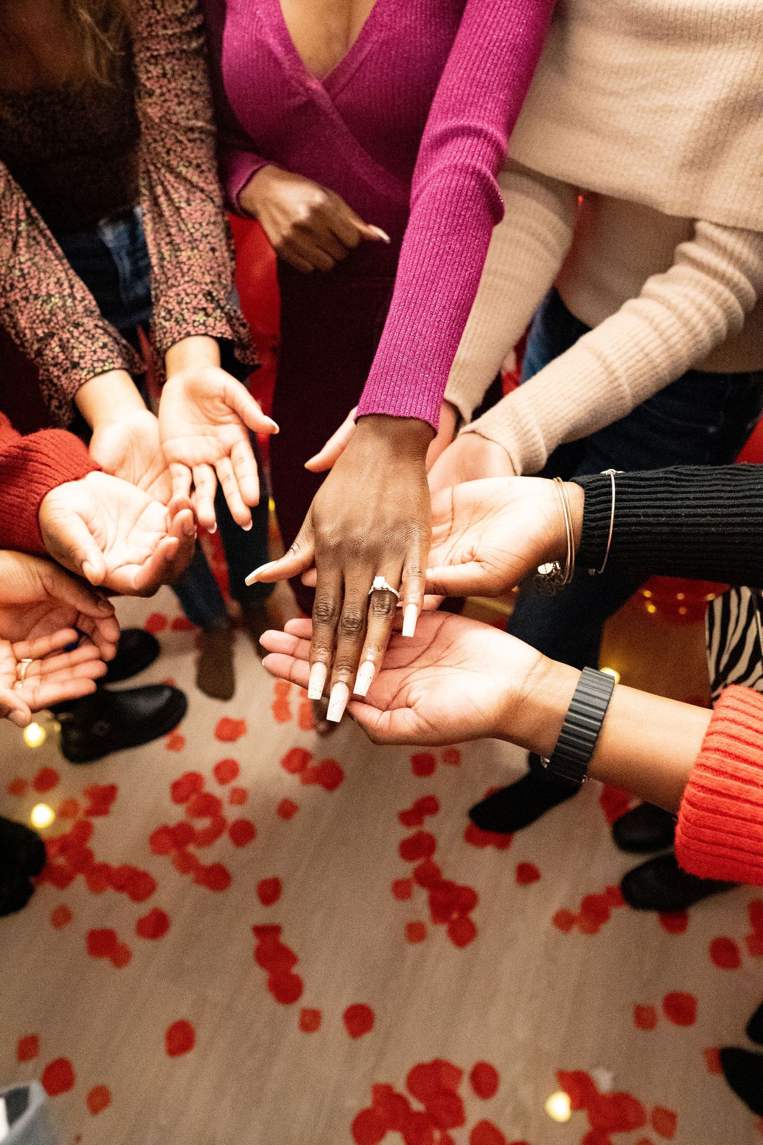 Hands holding small red heart-shaped objects in a sequence of connected images on a light floor.