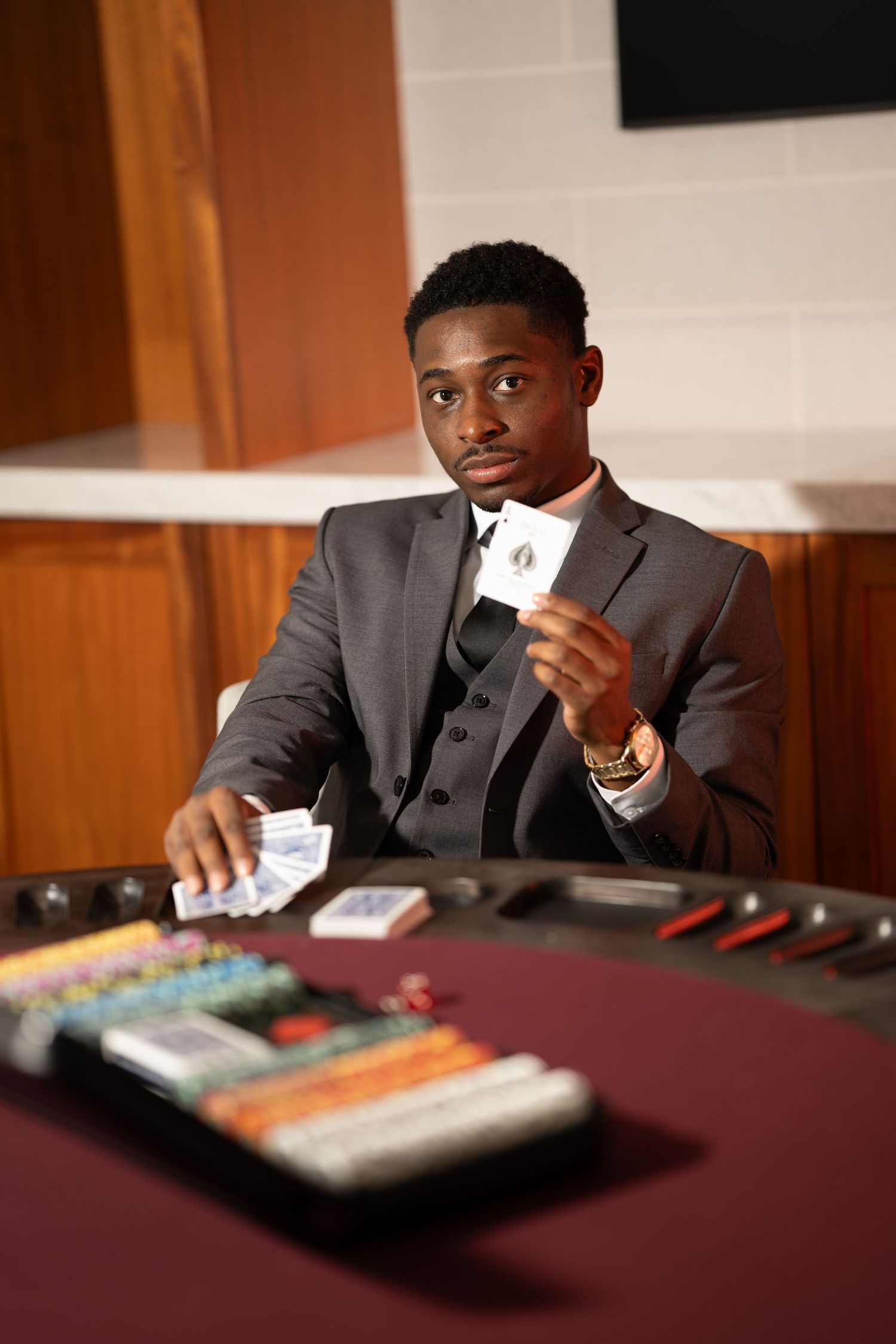 A person in a suit sits at a table with a thoughtful expression while holding a white card.