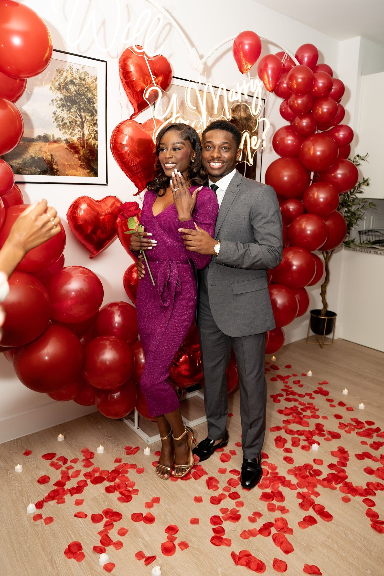 A romantic scene with red balloons and rose petals decorating a room while a couple celebrates a special moment.