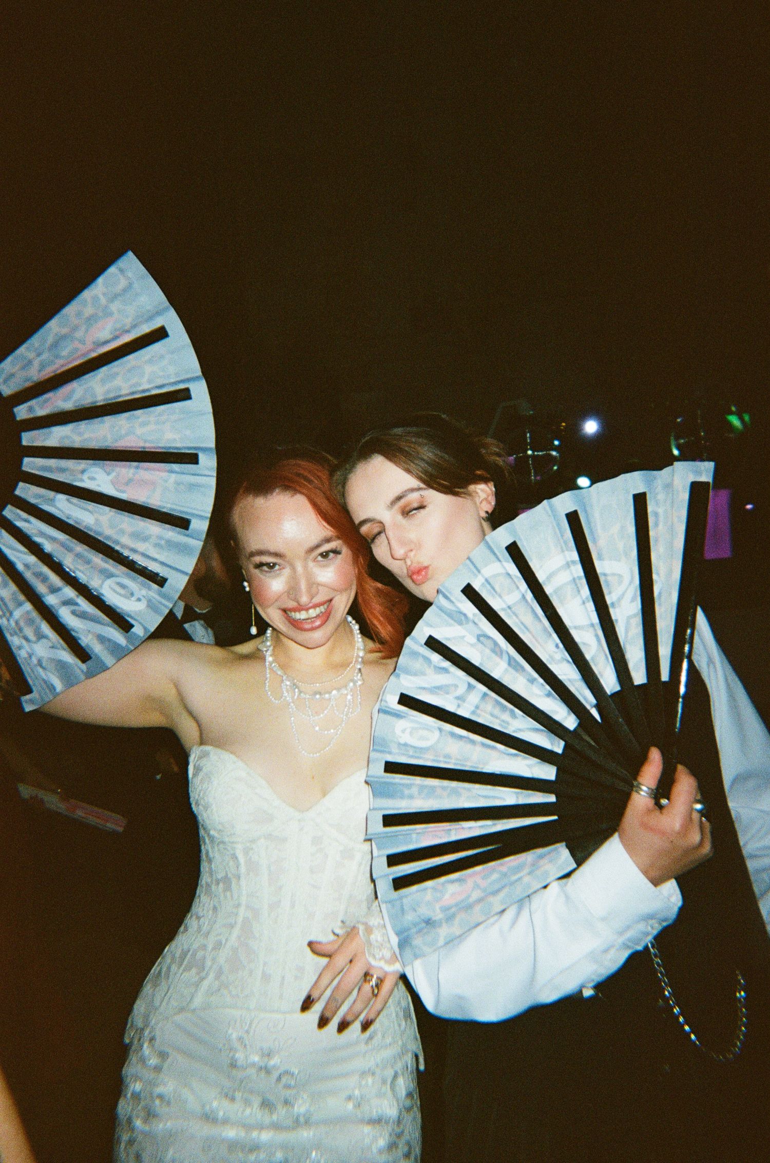 Two people at a formal event pose with decorative blue folding fans while wearing elegant attire.