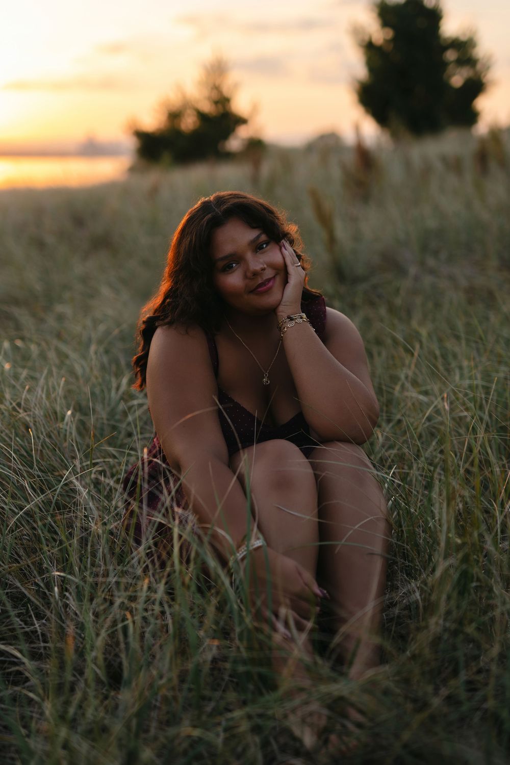 A silhouetted person poses playfully in tall grass during a warm sunset.
