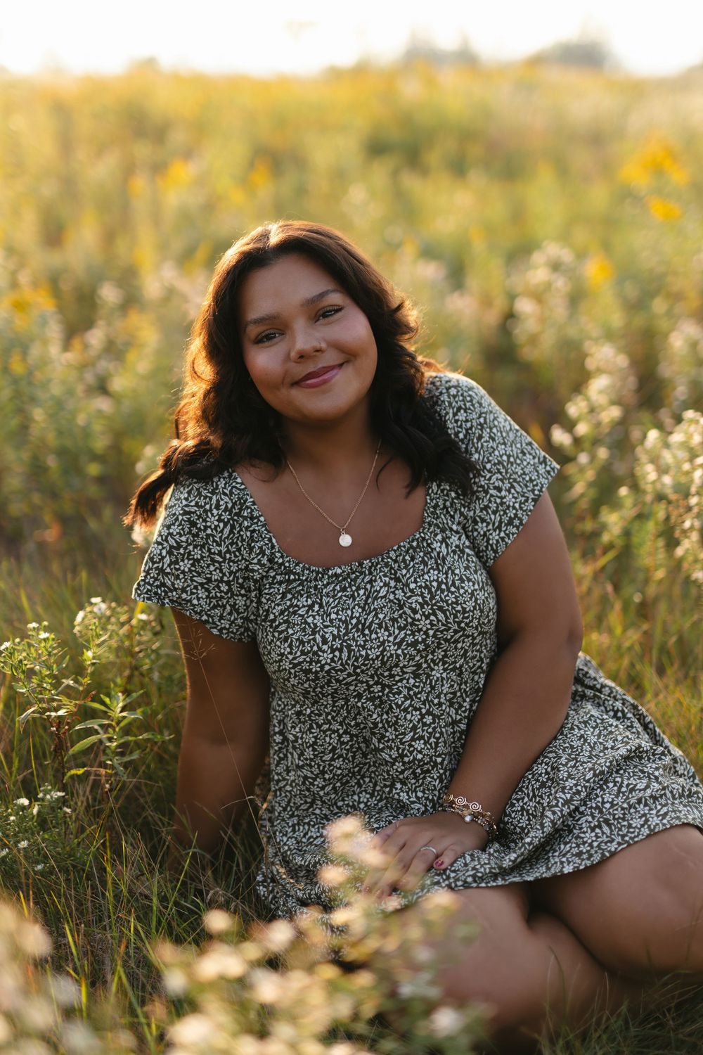 A person in a floral dress poses in a sunlit meadow with wildflowers during golden hour.