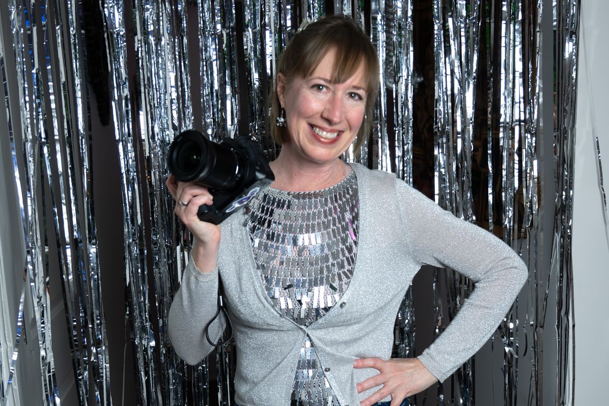 People wearing winter sweaters pose and smile in front of a sparkly silver backdrop at a festive party.
