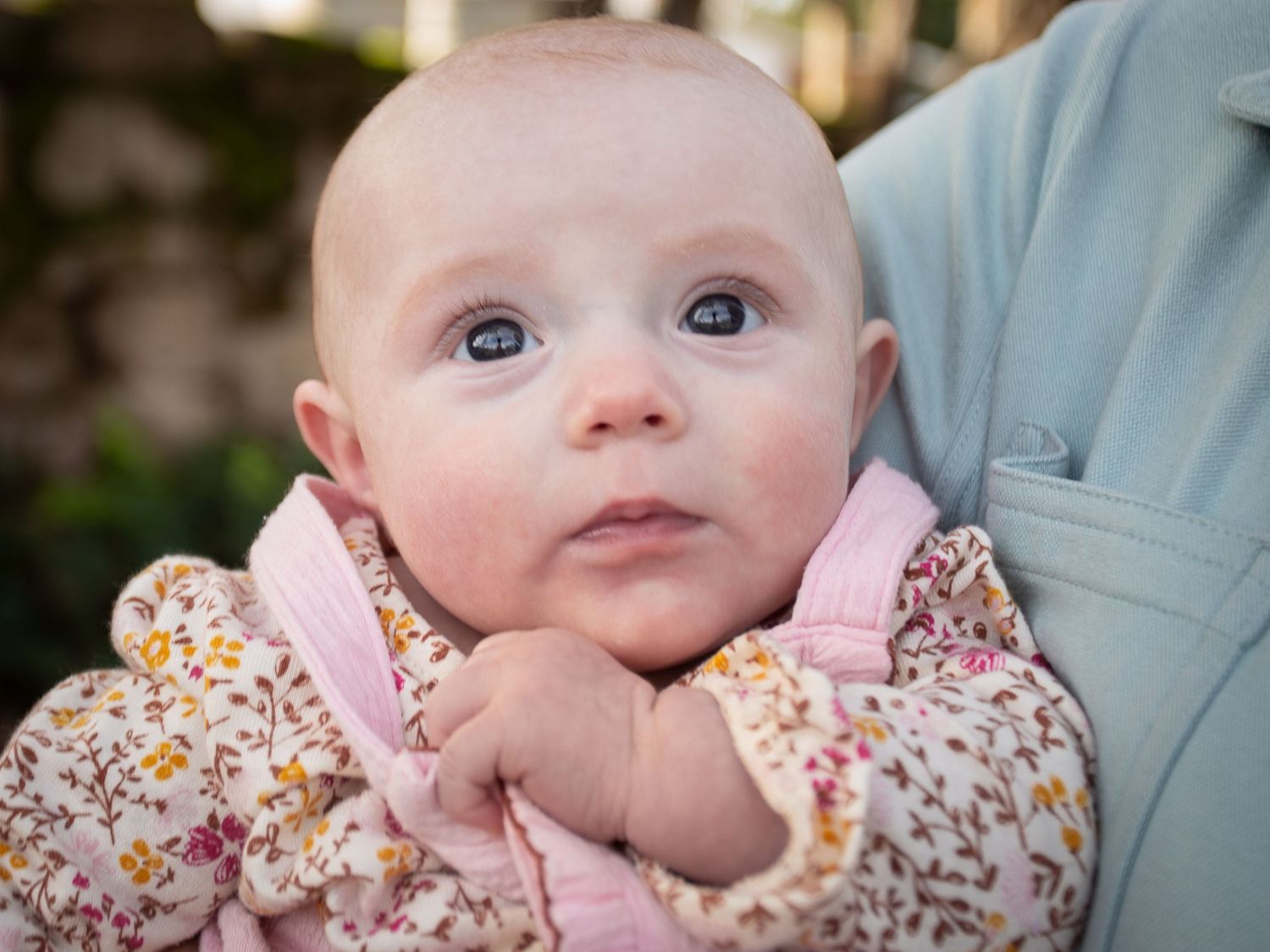 Baby wearing floral print dress with pink accents looks up with wide-eyed expression.