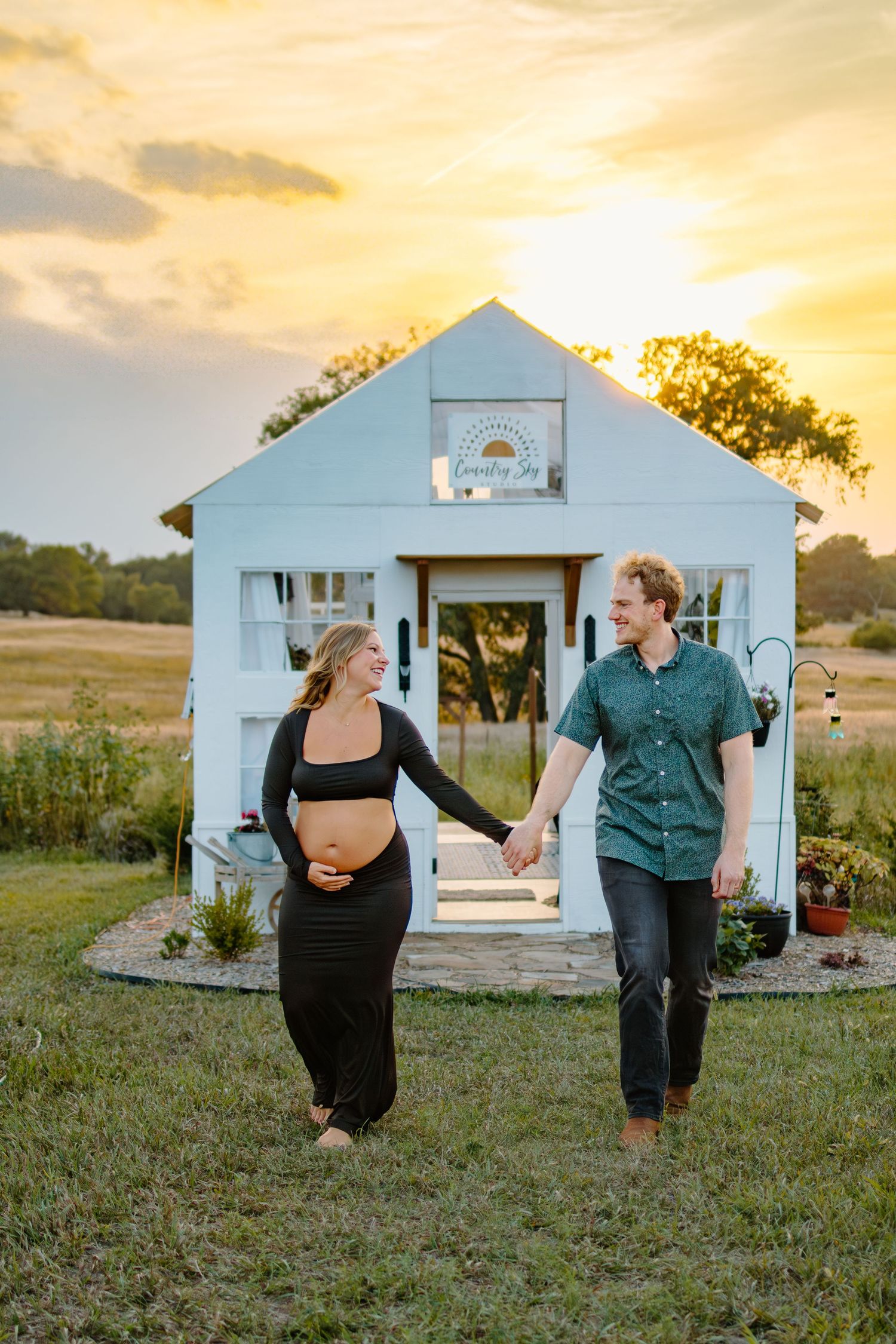 A couple dances playfully in front of a white chapel at sunset in a rustic outdoor setting.