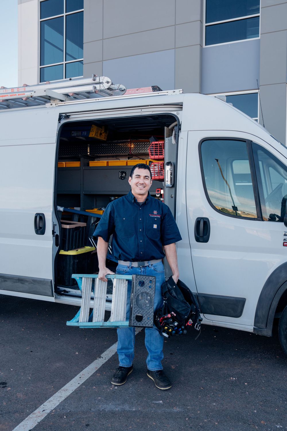 Service technician displays equipment next to white commercial van in parking lot.