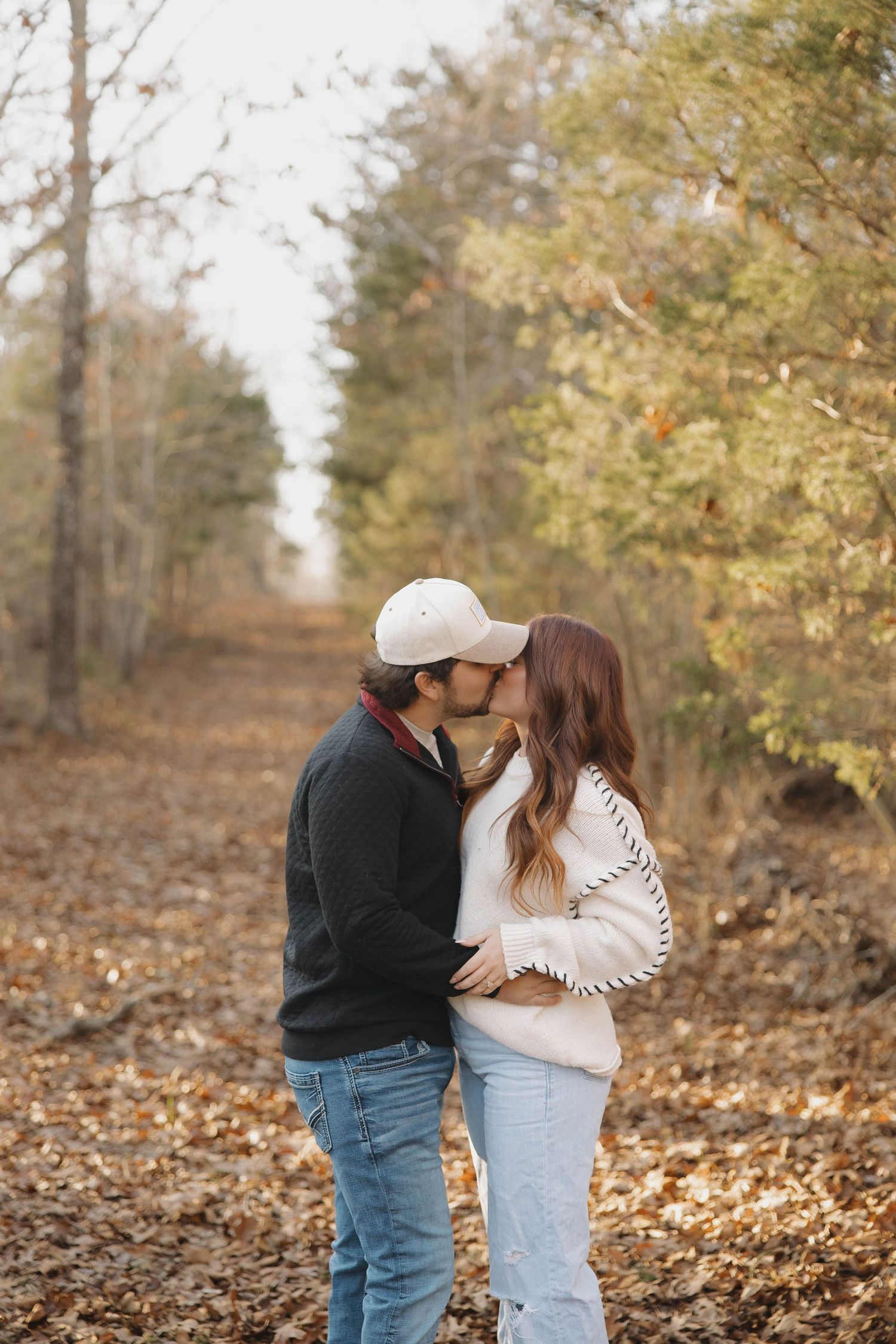A couple shares a romantic moment among fallen autumn leaves in a wooded area.