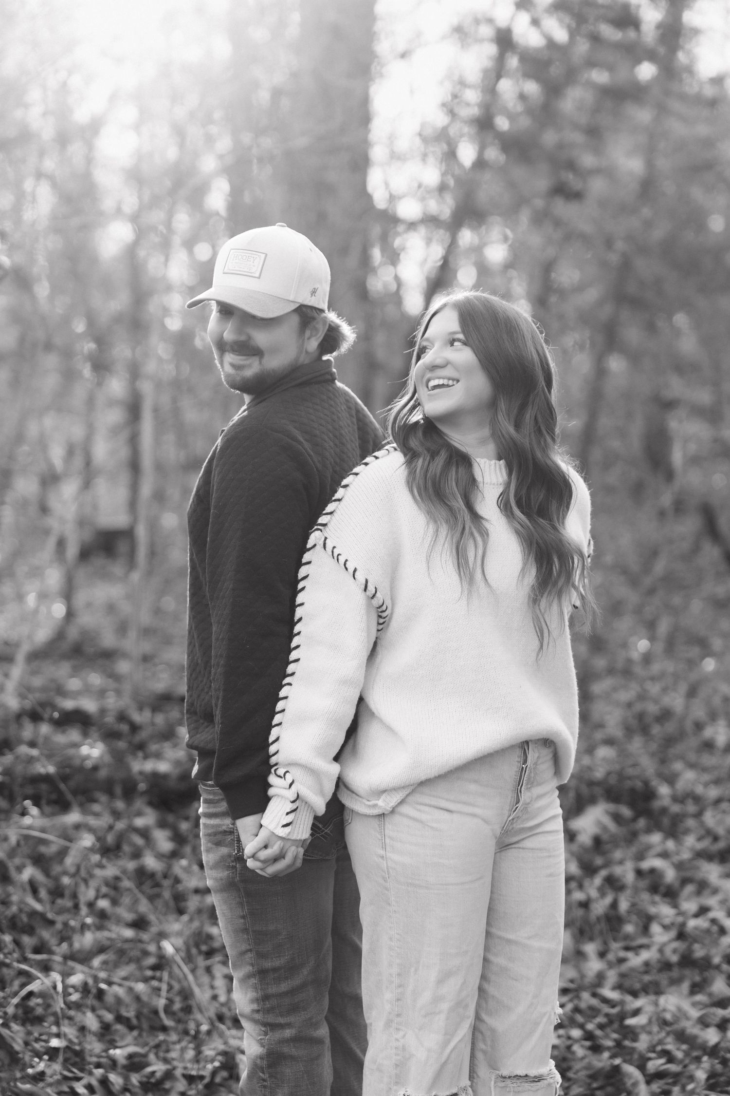 A couple shares intimate moments in a wooded forest setting captured in black and white photography.