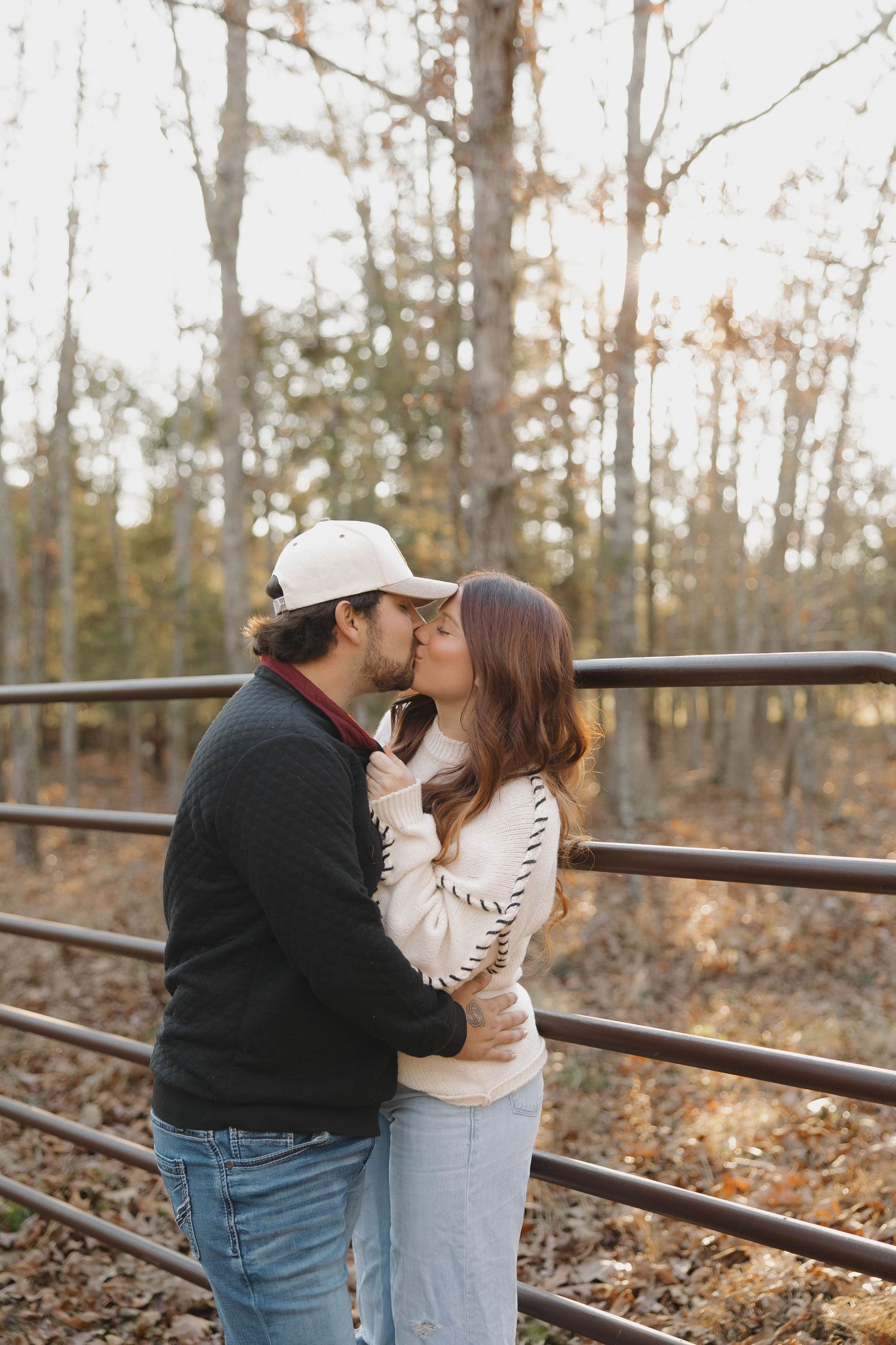 A couple shares a tender moment by a rustic wooden fence in an autumn forest setting.