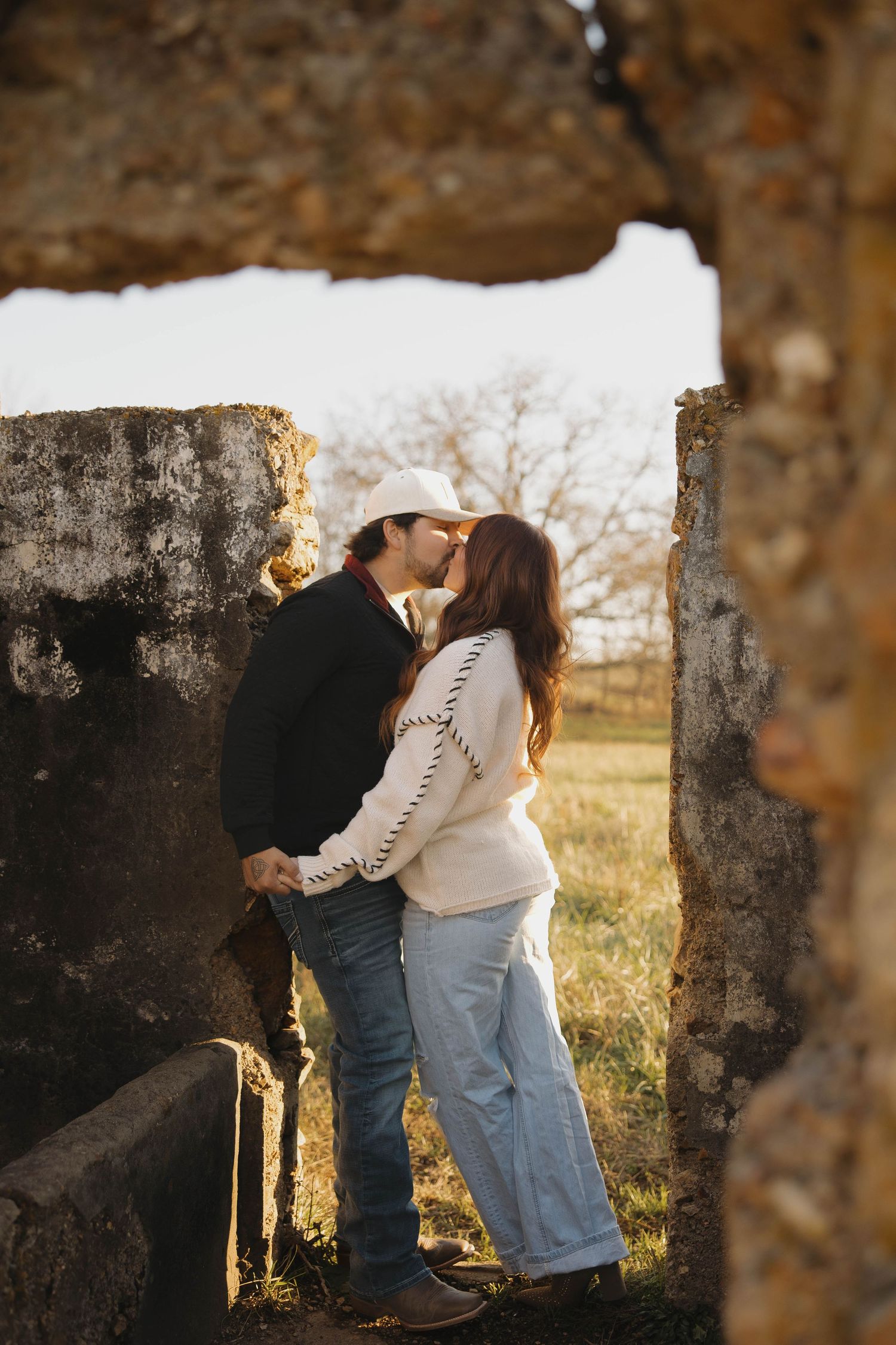 A couple embraces in a romantic outdoor setting during golden hour with trees framing the scene.