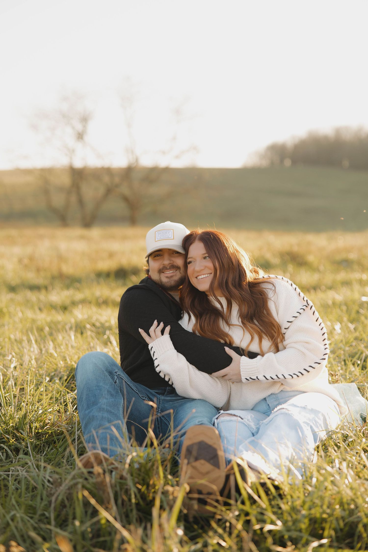 A couple lies together intimately in a sunlit meadow with tall grass during golden hour.