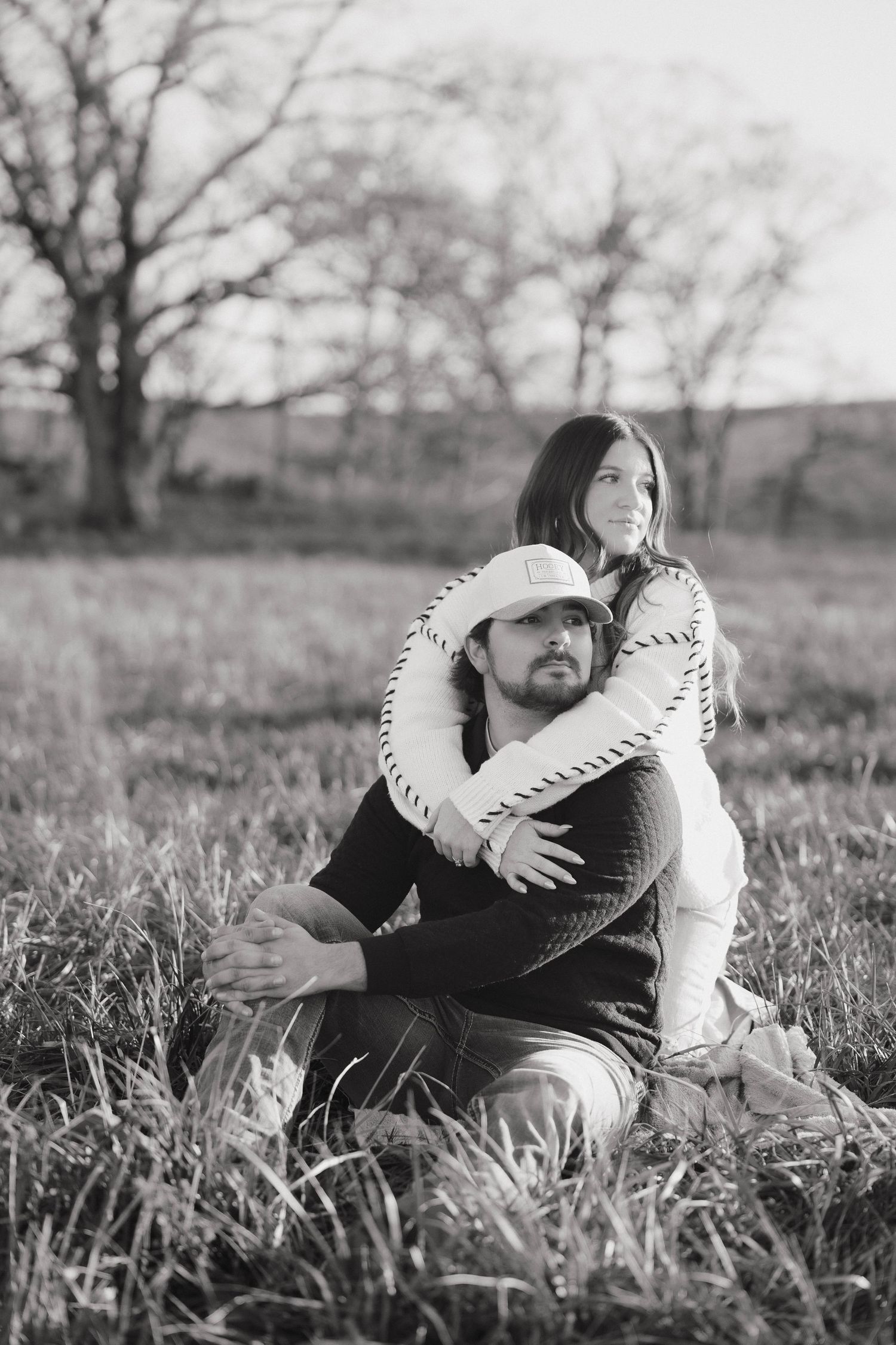 A black and white photo captures an intimate moment between a couple in a grassy field.