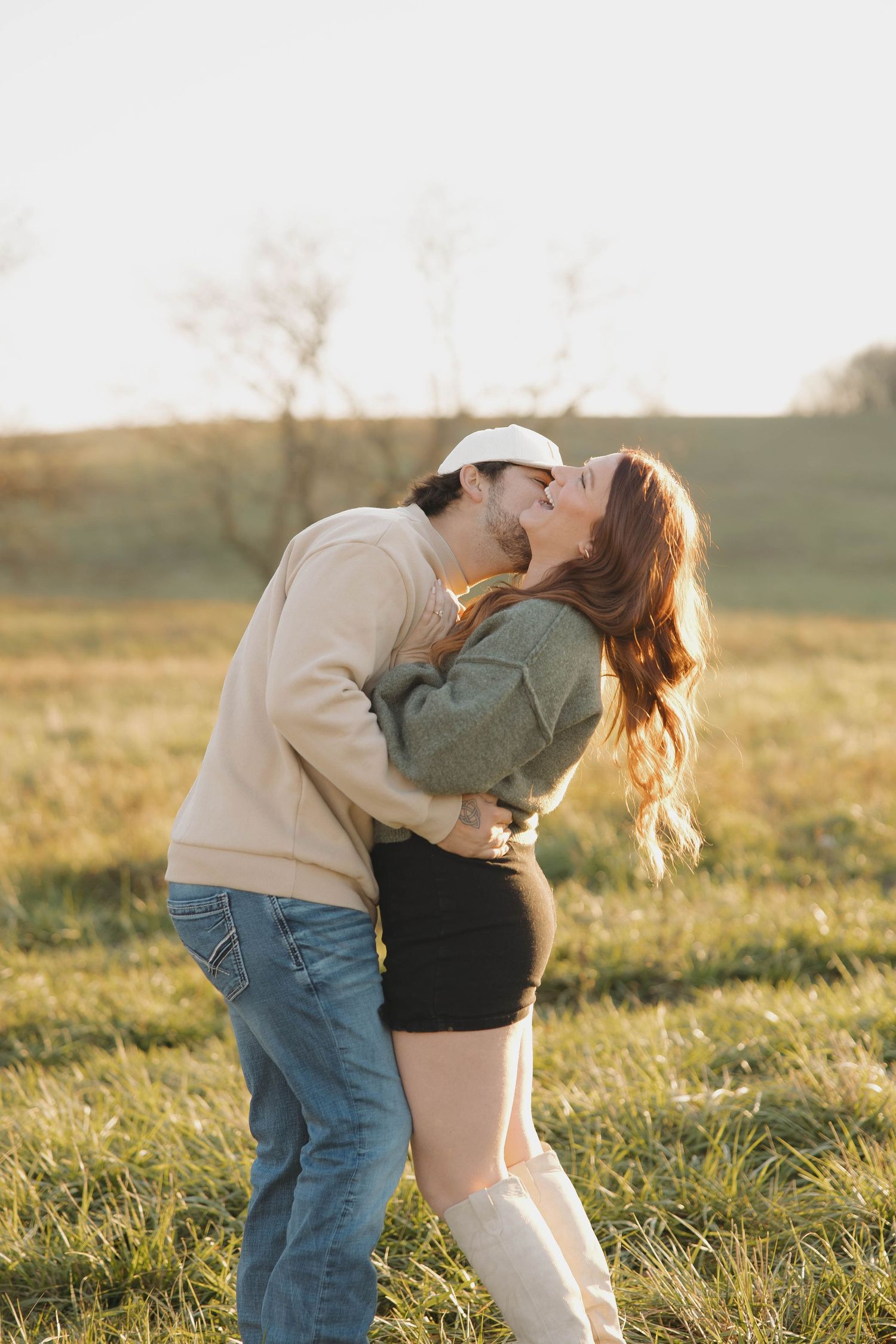 A couple dances and embraces in a sunlit meadow during golden hour, creating a romantic silhouette against the landscape.