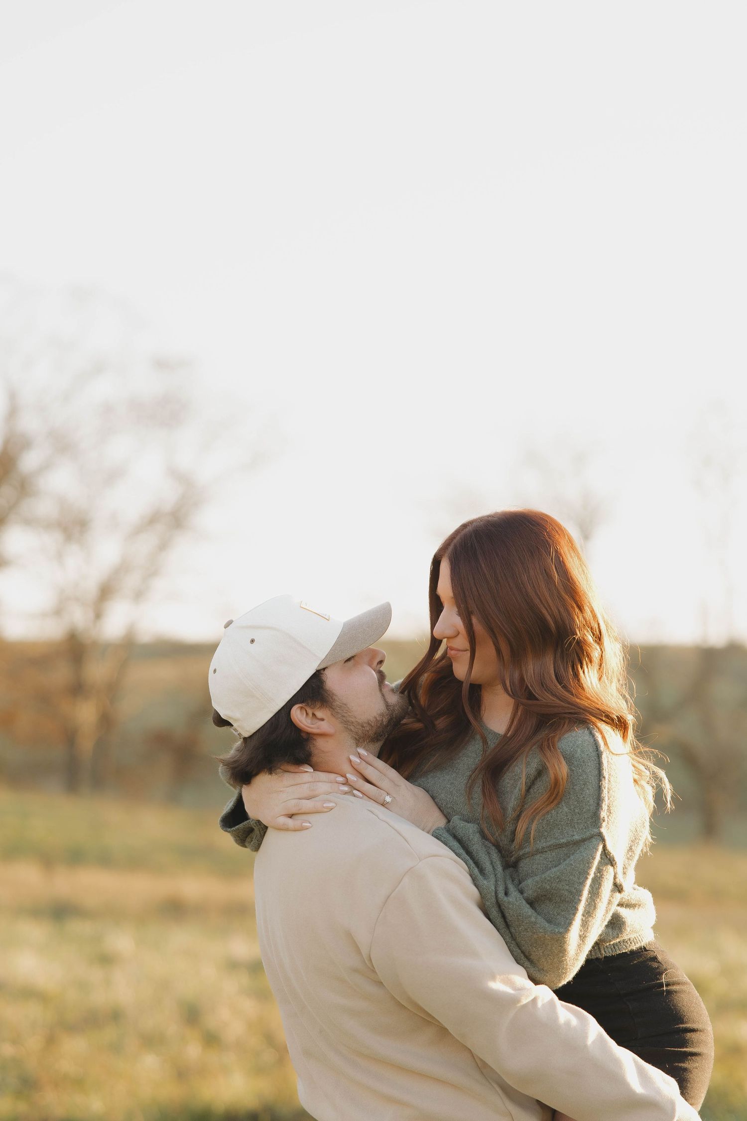 A romantic moment captured between two people in casual attire sharing an intimate embrace in a grassy field at sunset.