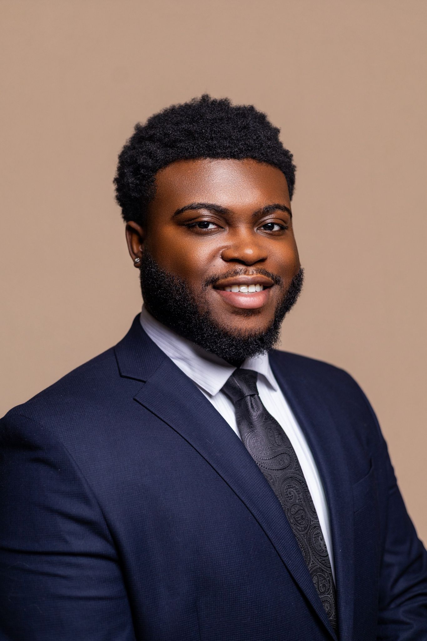 Professional headshot series of a person in a navy suit and tie against a neutral backdrop.