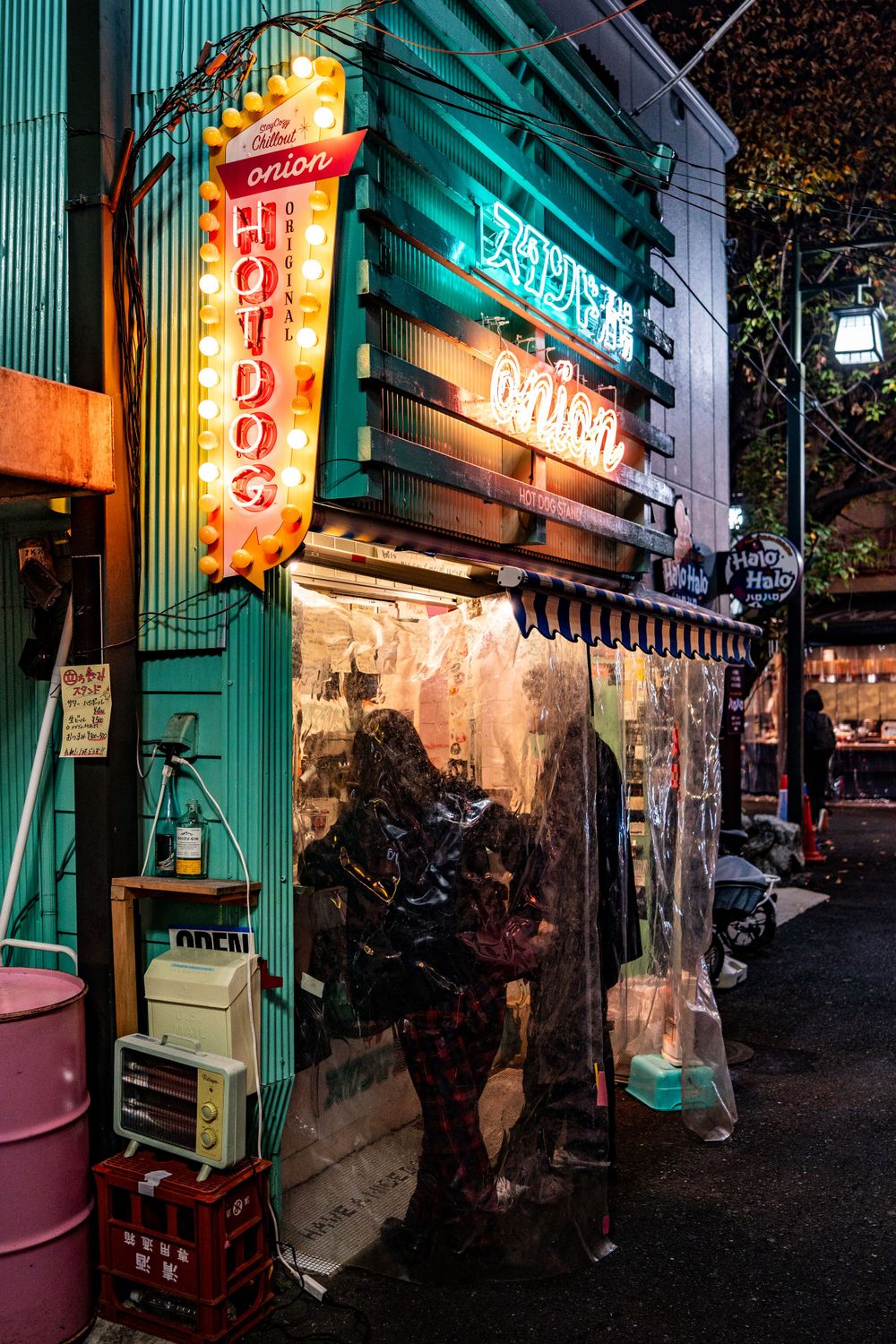 Vintage neon signs illuminate the entrance of a traditional Japanese hot dog stand at night.