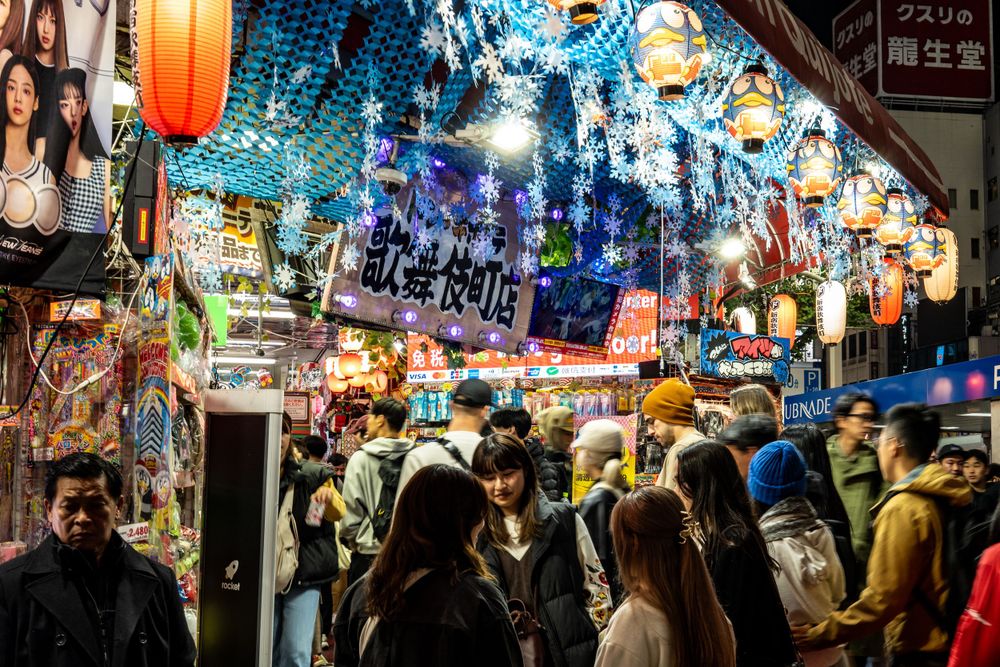 Crowded marketplace in Japan with colorful lanterns and decorations hanging overhead.