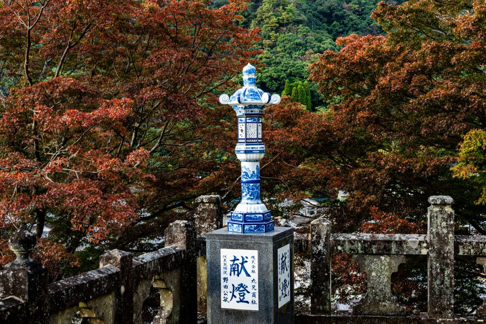Traditional blue and white stone lantern among autumn maple trees at Japanese temple.