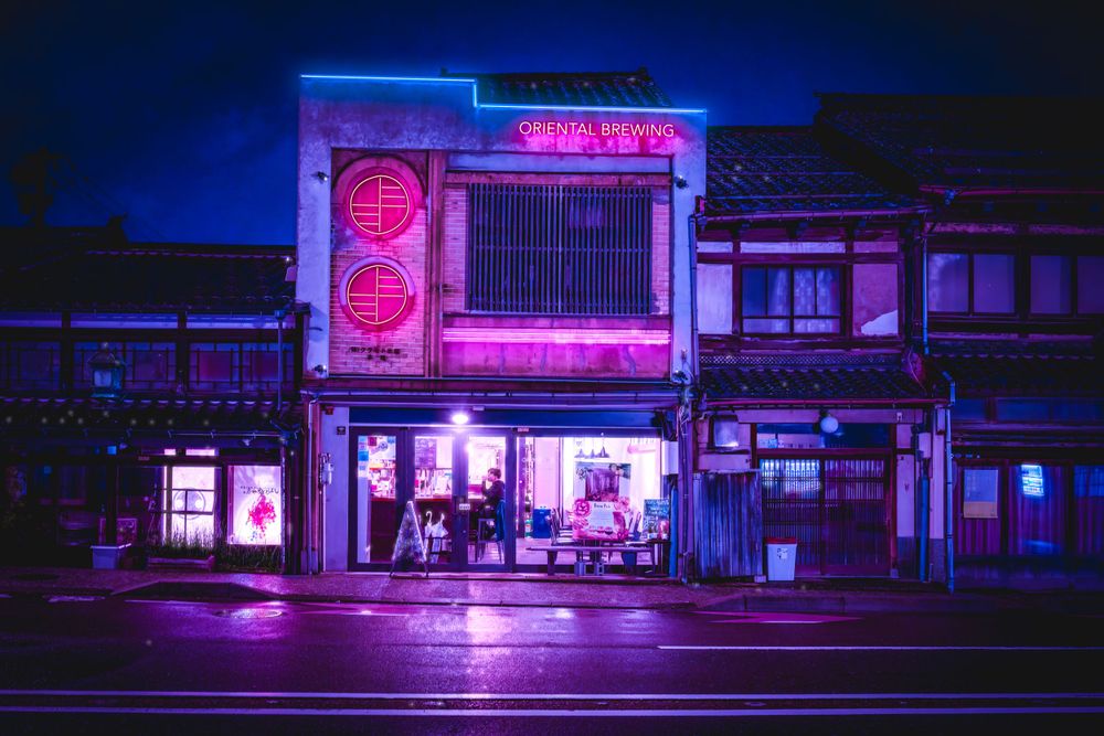 Neon-lit storefront with purple lighting illuminates a street in an Asian district at night.