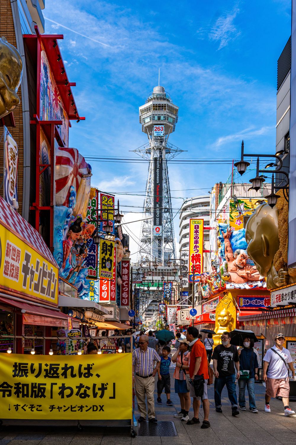 Bustling street in Osaka's Shinsekai district with the iconic Tsutenkaku Tower rising in the background.