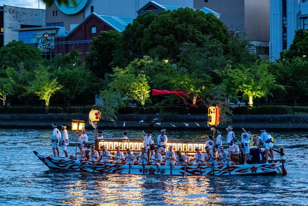 Traditional Japanese lantern-lit boats gathering on a river at dusk during a summer festival.
