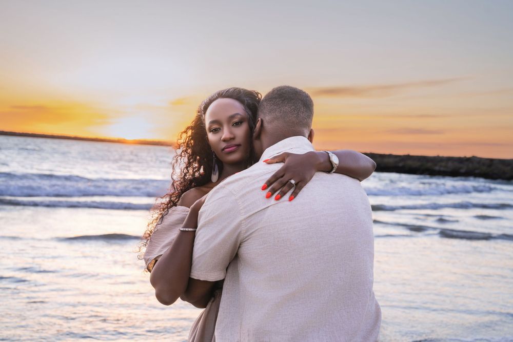 Tender embrace between couple on beach with dramatic sunset over ocean waves.