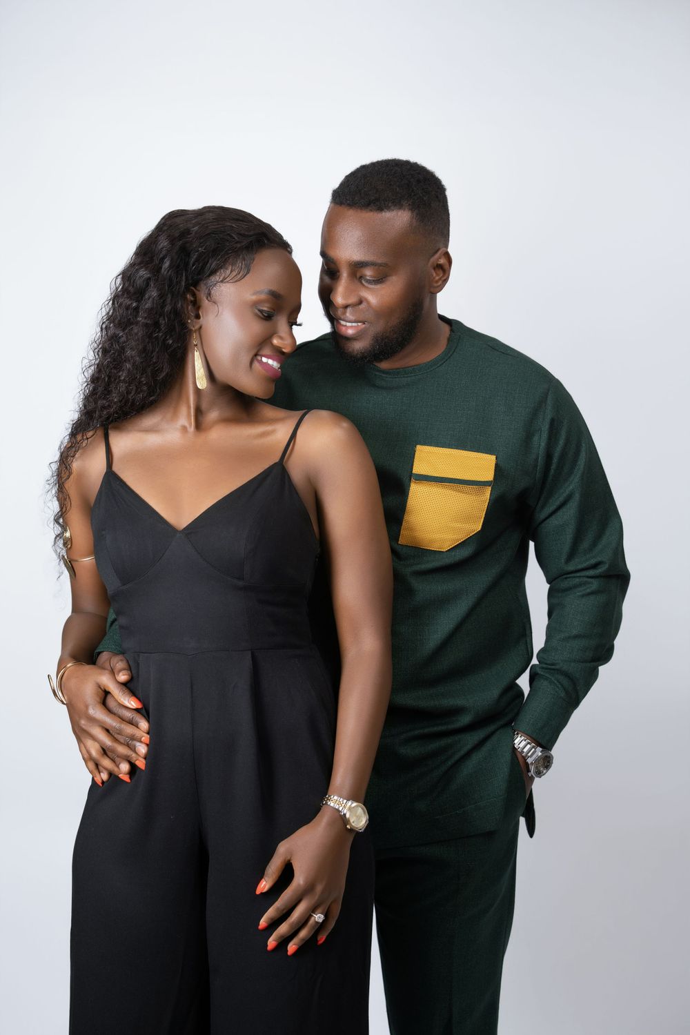 Loving couple in studio shot wearing black dress and green outfit with yellow pocket detail.