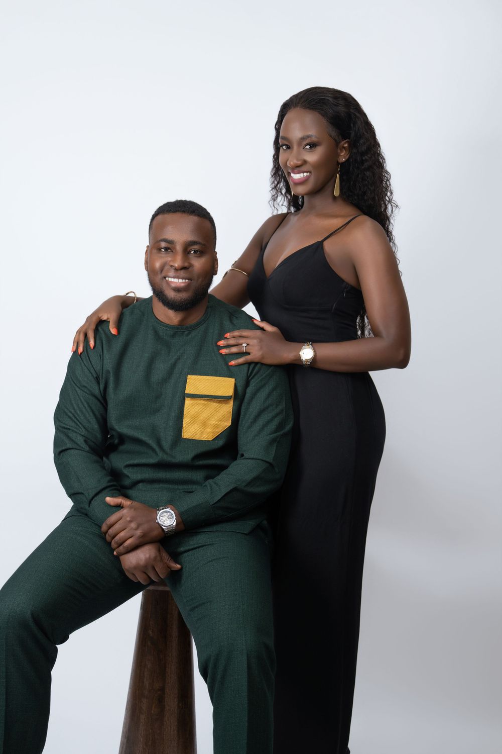 Elegant couple in studio wearing black gown and green traditional suit with yellow accent.