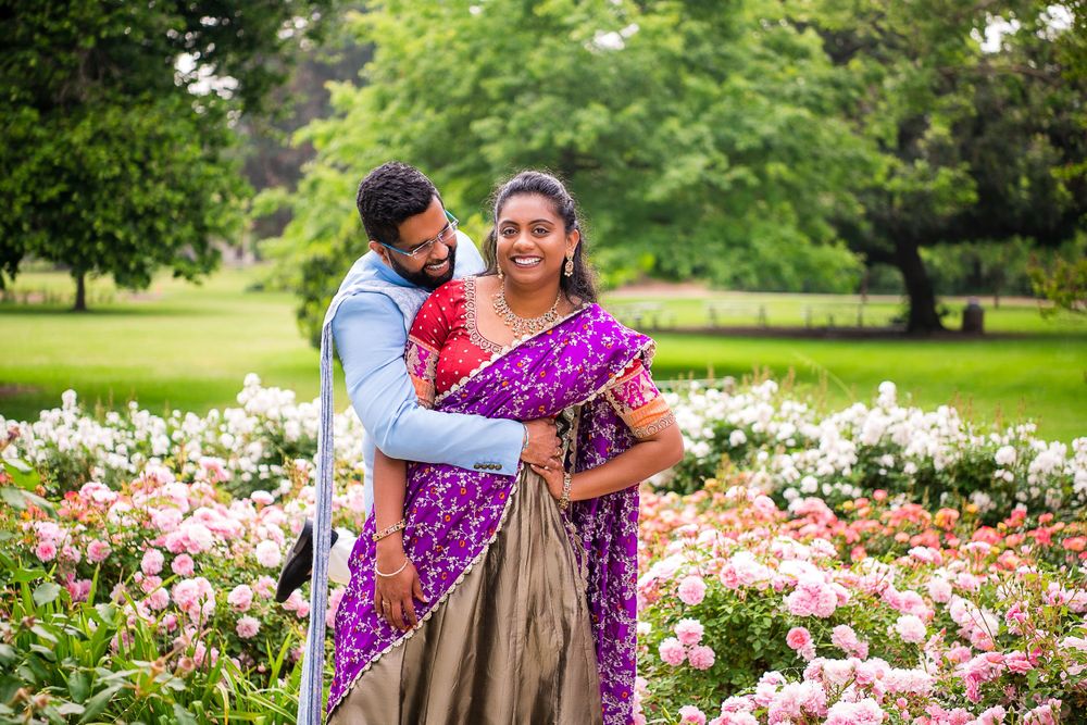 A couple poses together in a vibrant garden filled with pink flowers.