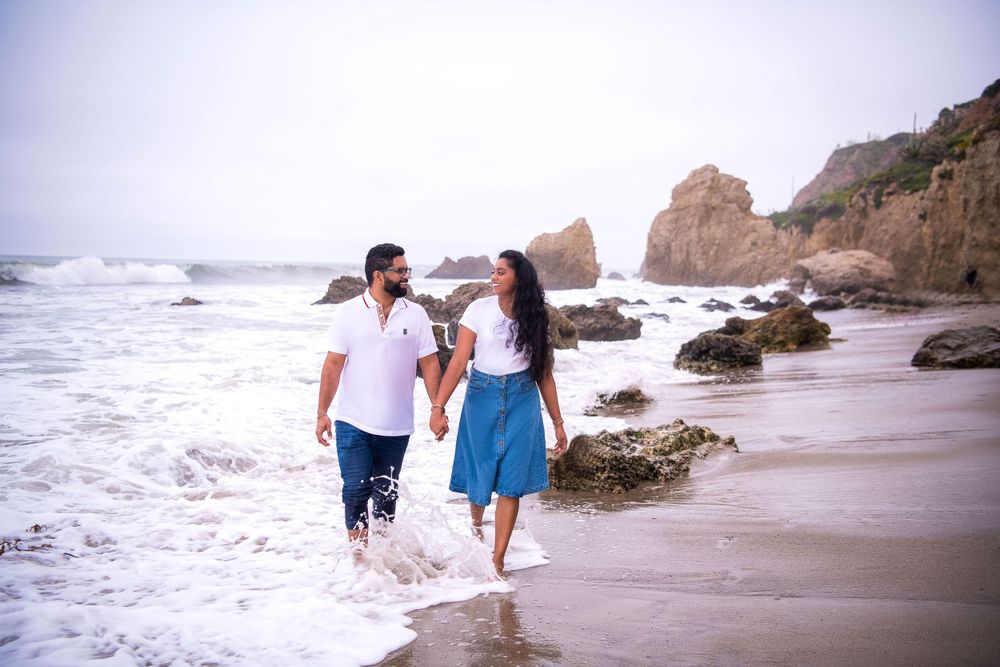 A couple enjoying a walk along the shoreline with waves crashing nearby.