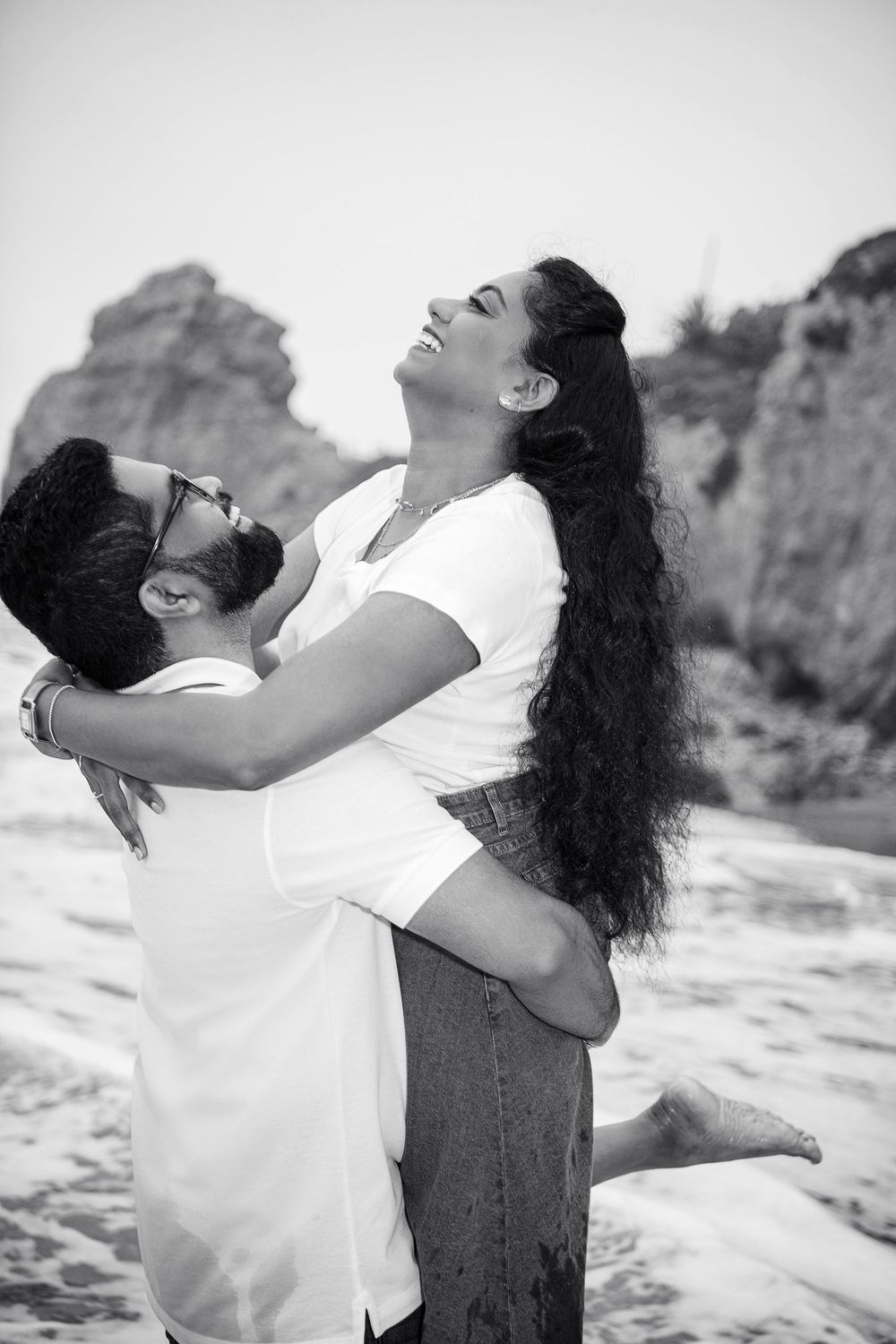 A playful black and white beach portrait with dramatic rock formations.