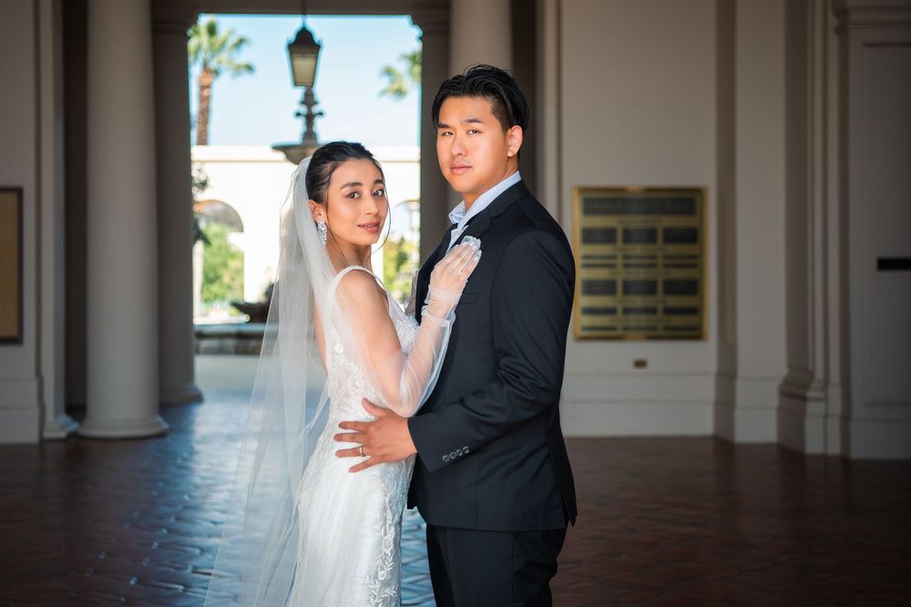 Elegant couple in wedding attire pose together in a covered walkway.