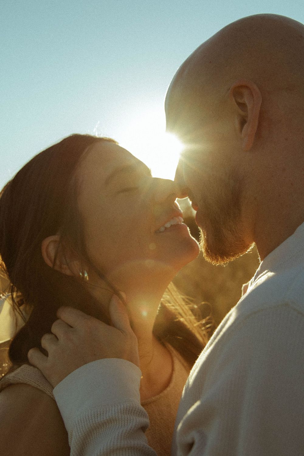 Couple sharing a romantic kiss backlit by bright golden sunlight outdoors.