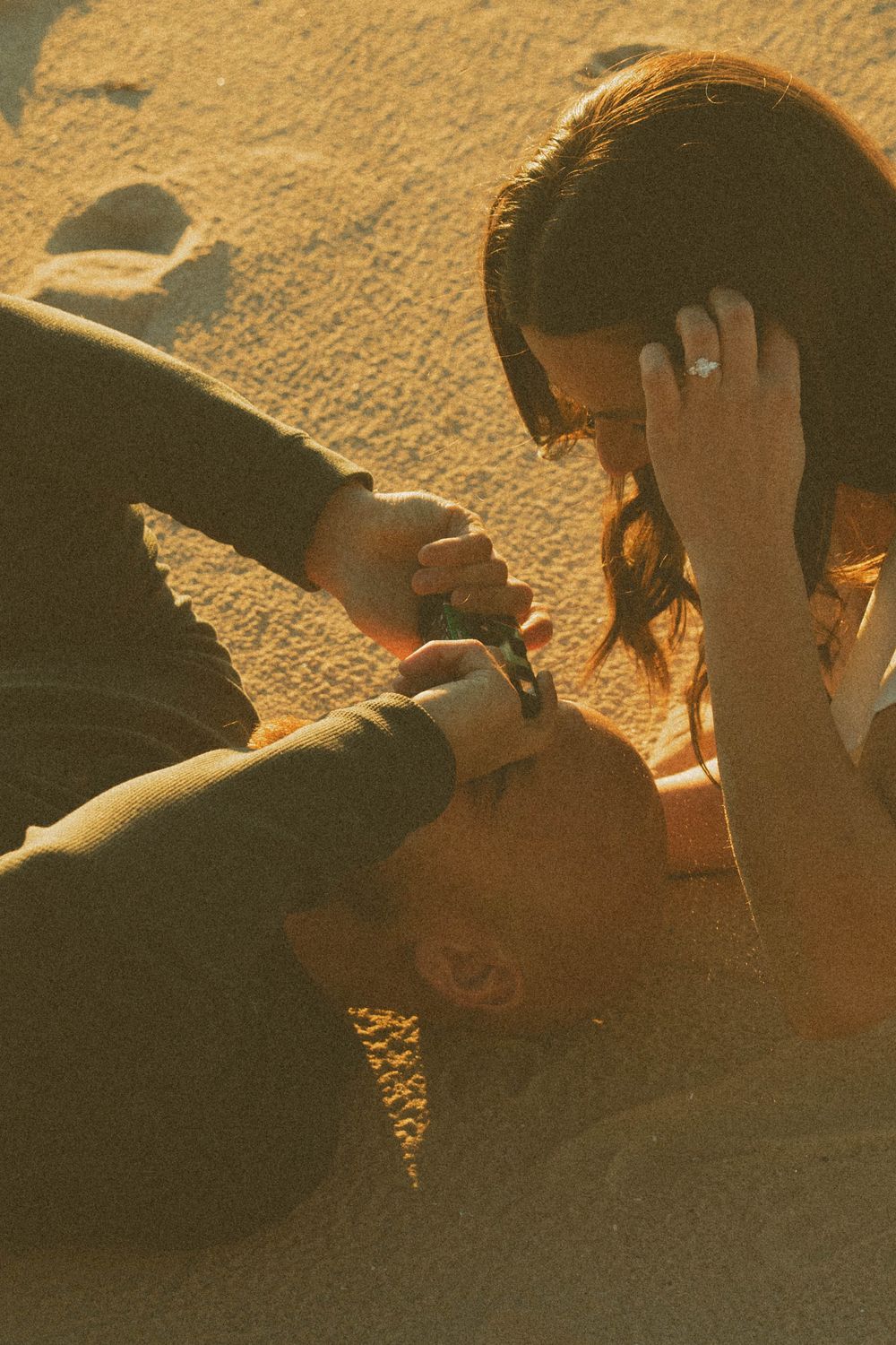 Couple sharing an intimate moment lying on sandy beach at golden hour sunset.