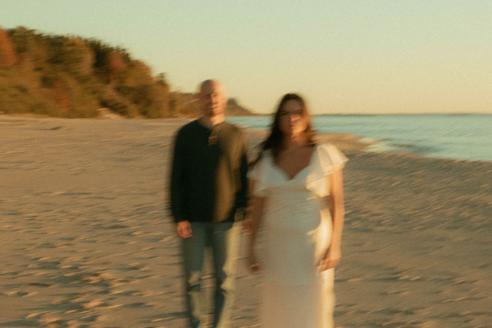 Bride and groom walking hand in hand on a beach at golden sunset.