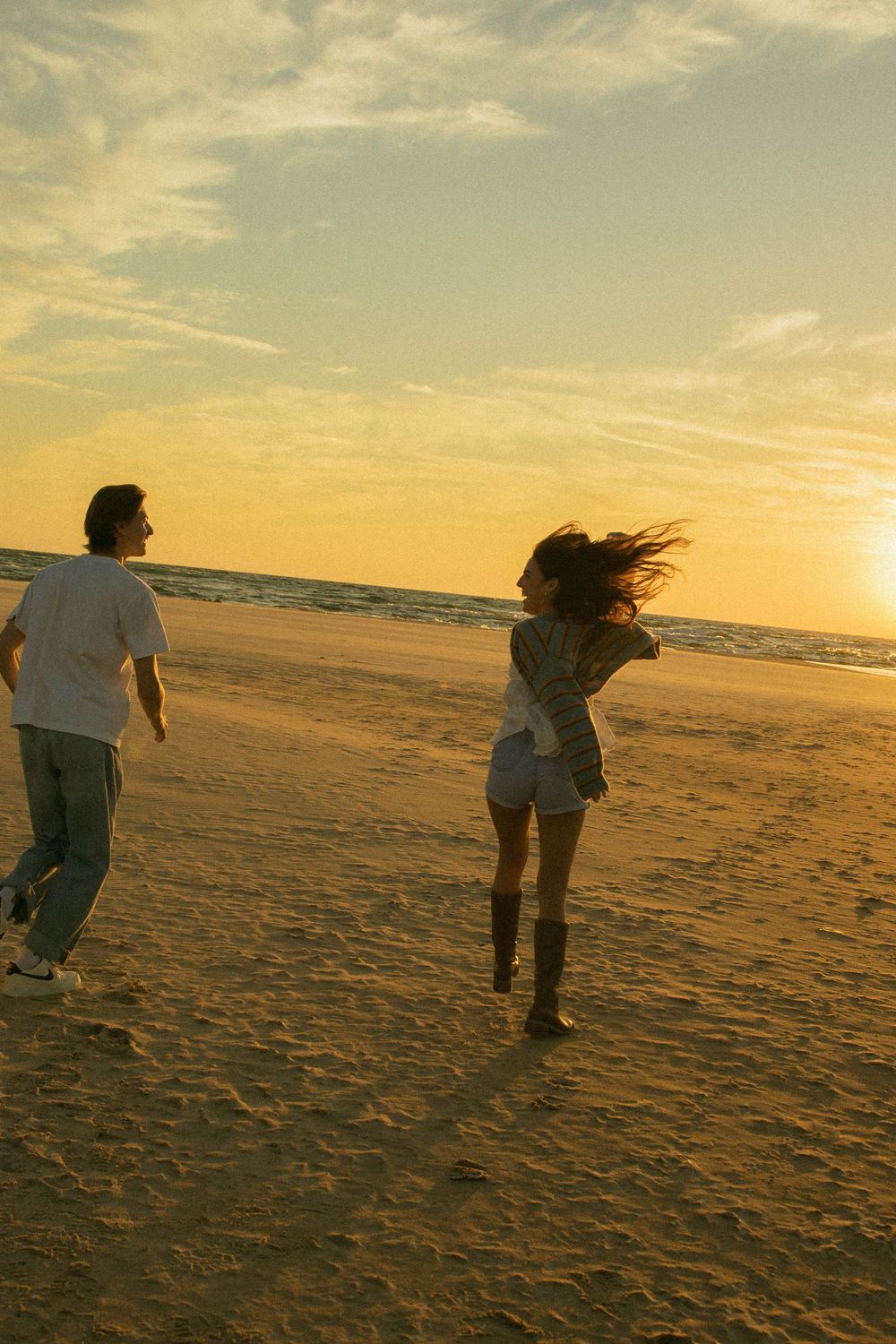 Couple running playfully on a sandy beach during a vibrant golden sunset.