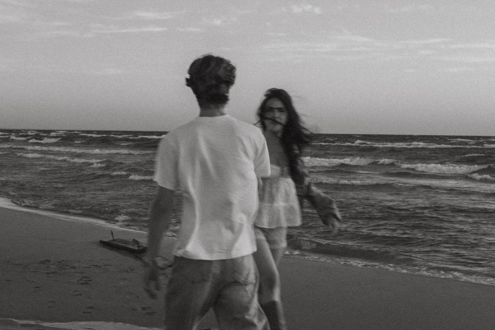 Black and white photo of a couple walking along a breezy ocean shoreline.