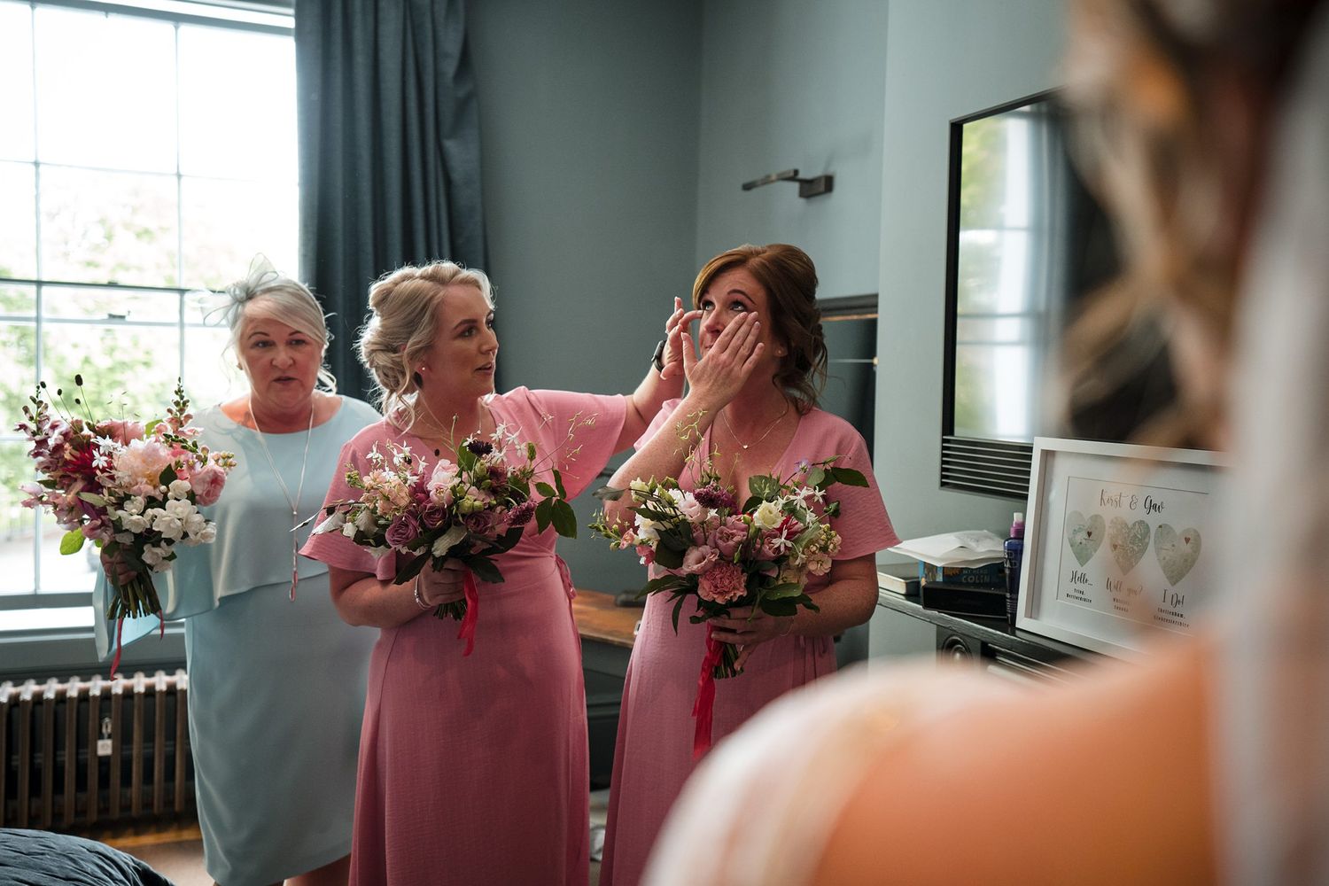 Bridesmaids in pink and blue dresses share a laugh while holding floral bouquets during a wedding preparation moment in Halifax, Nova Scotia