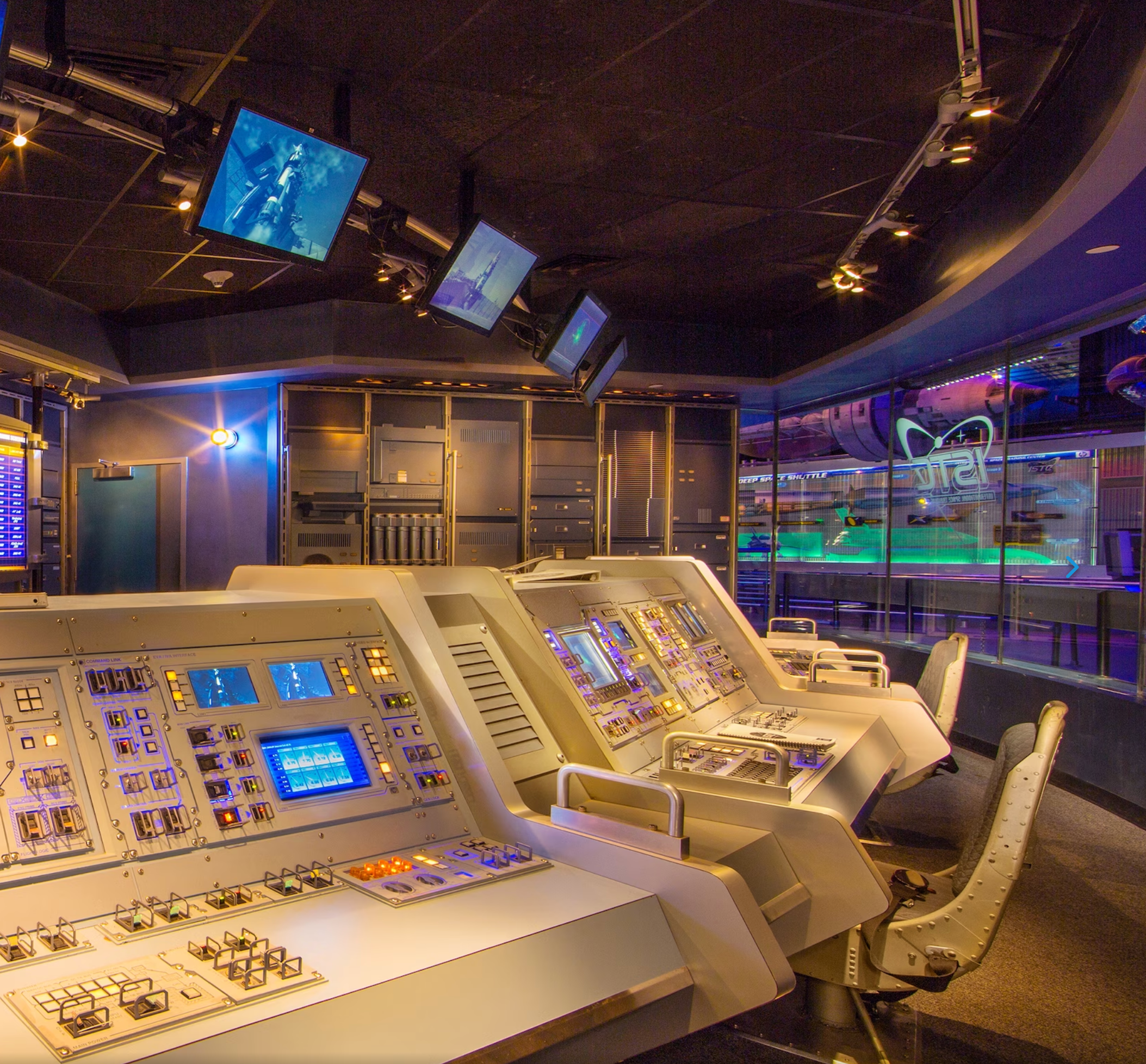 A panoramic view of a vintage control room with multiple illuminated control panels and monitoring displays.