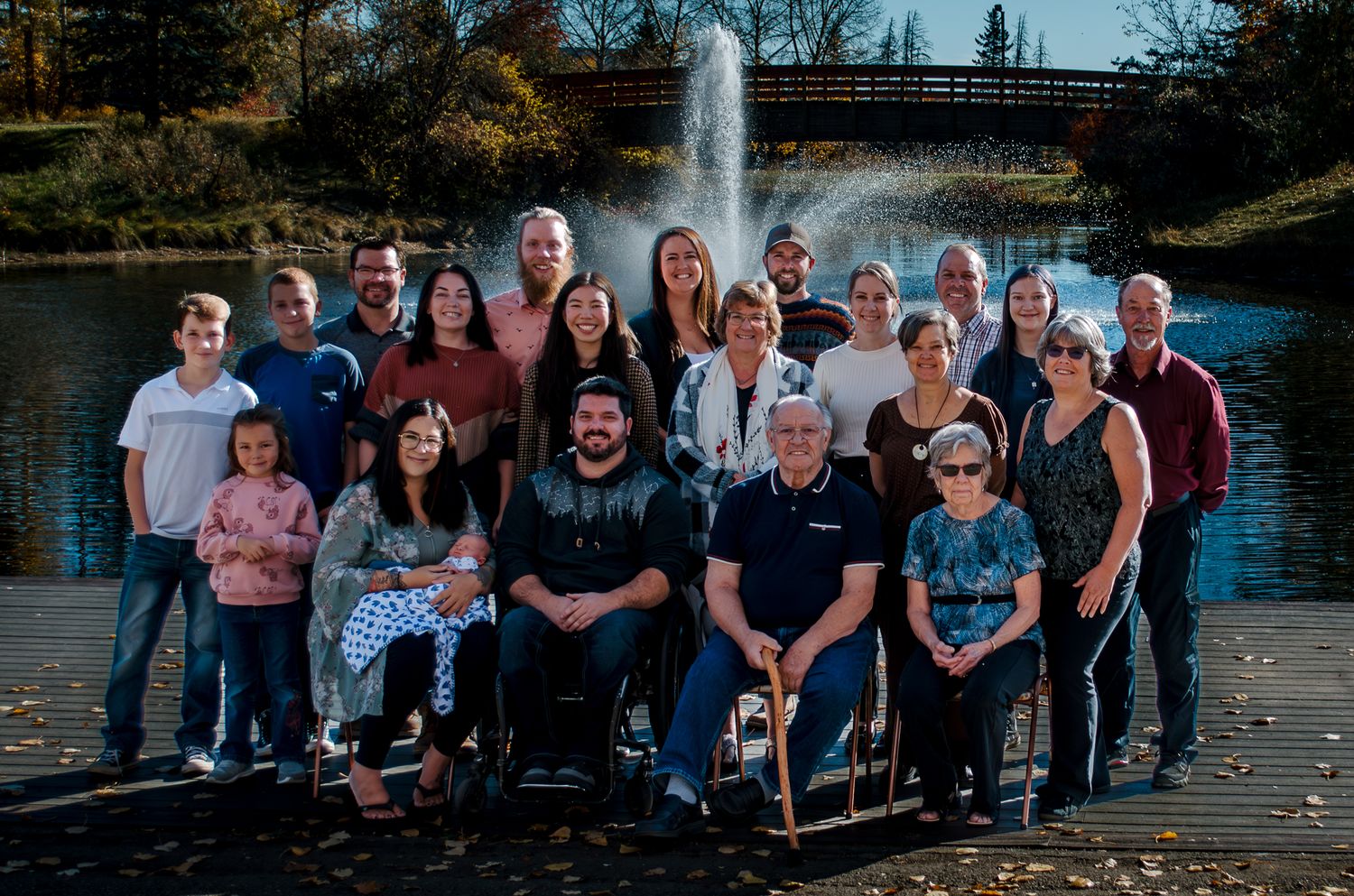 Large family group photo taken outdoors with fountain and autumn trees in background.