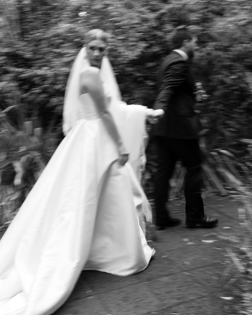 Black and white artistic photo of newlyweds walking along a garden path.