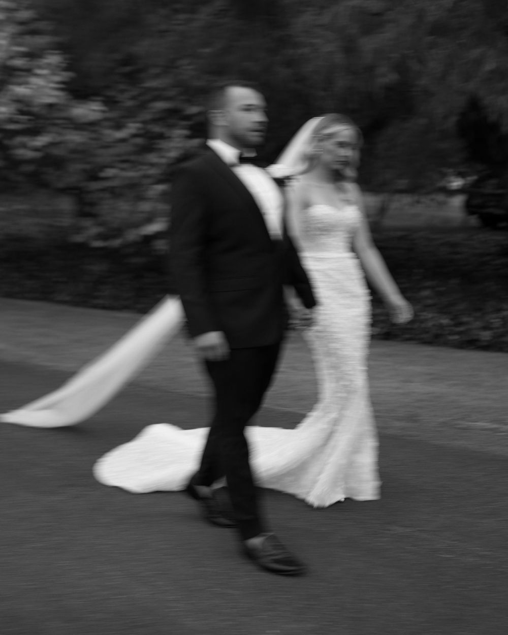 Black and white candid photo of a couple walking outdoors in formal wedding attire.