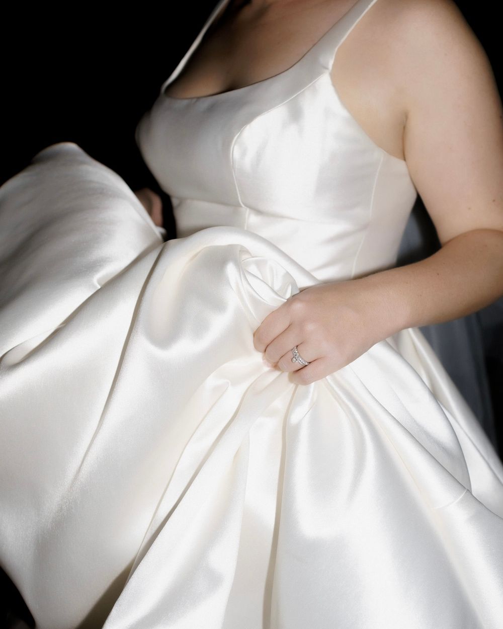 A close-up view of an elegant white satin wedding dress with structured pleating details.