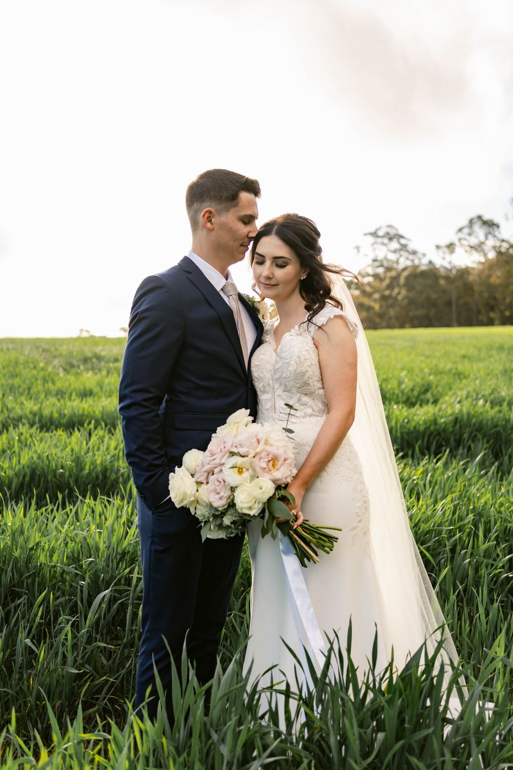Romantic wedding portrait of couple standing in tall grass field at golden hour.