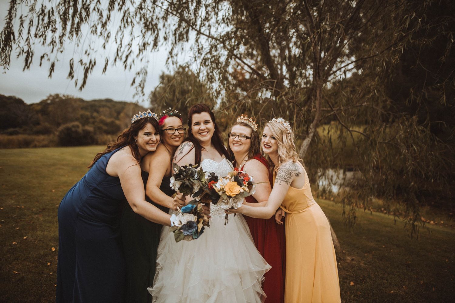 Wedding party celebrates outdoors under willow trees at sunset.