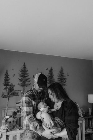 Black and white image shows a family spending time together in a room with pine tree wall decor.
