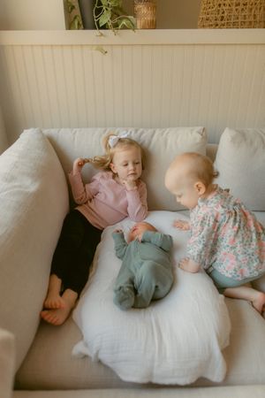 Children lounging together on a white couch with beadboard wall and decorative accents in the background.