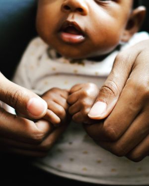 Close up of a baby's hand being gently held by an adult's hands in a tender moment.