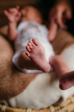 Close up of tiny infant feet resting on a woven surface with soft lighting and blurred background.