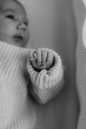 A black and white close-up of a tiny baby's hand grasping a knitted sweater sleeve.